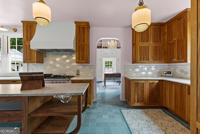 kitchen featuring brown cabinetry, backsplash, decorative light fixtures, light countertops, and custom exhaust hood