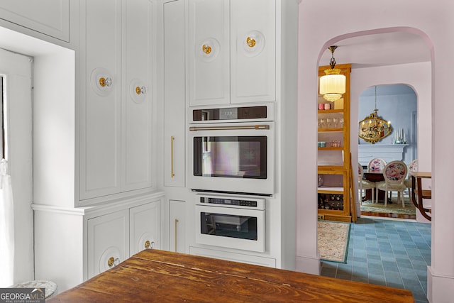 kitchen with arched walkways, dark countertops, an inviting chandelier, and double oven