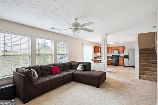 living area featuring light carpet, a ceiling fan, ornate columns, visible vents, and stairway