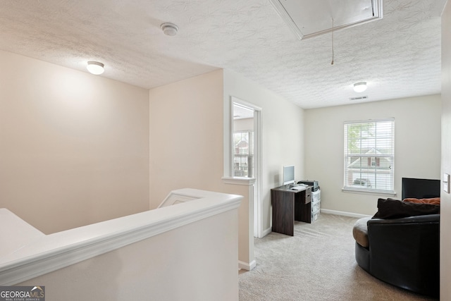 living area featuring light colored carpet, attic access, a textured ceiling, and baseboards