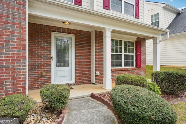 view of exterior entry featuring brick siding and covered porch