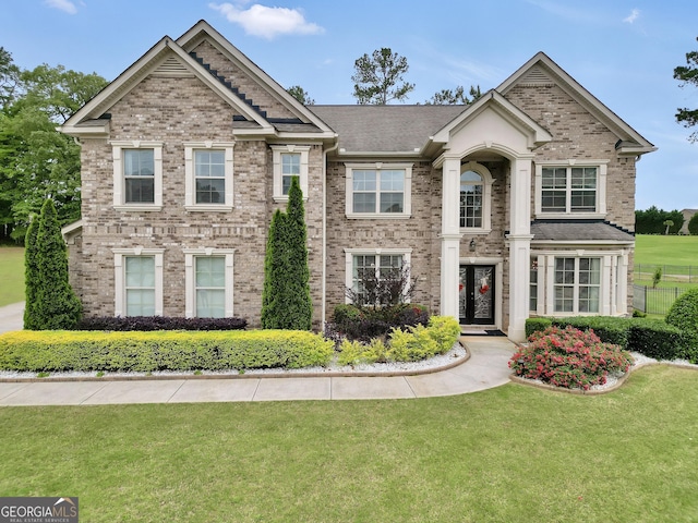 view of front facade featuring brick siding, fence, and a front yard