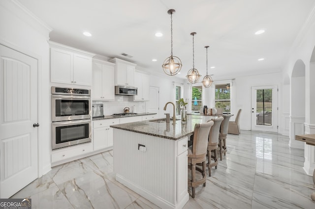 kitchen featuring a center island with sink, a sink, dark stone countertops, marble finish floor, and stainless steel appliances