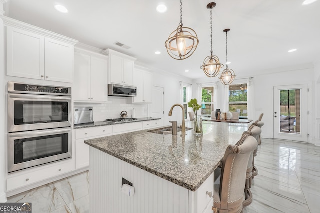 kitchen featuring an inviting chandelier, marble finish floor, an island with sink, a sink, and stainless steel appliances