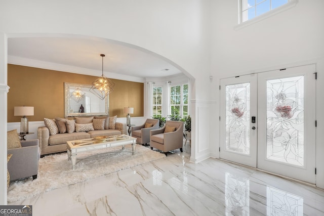 living area with crown molding, marble finish floor, a towering ceiling, french doors, and arched walkways