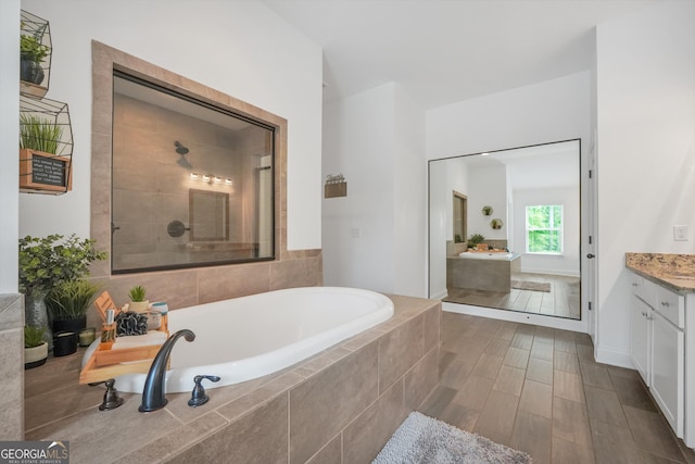 bathroom with a tile shower, a bath, and vanity
