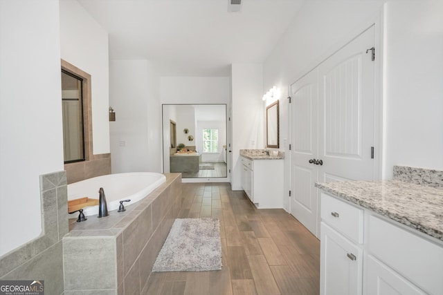 full bath featuring a sink, two vanities, a bath, and wood finished floors