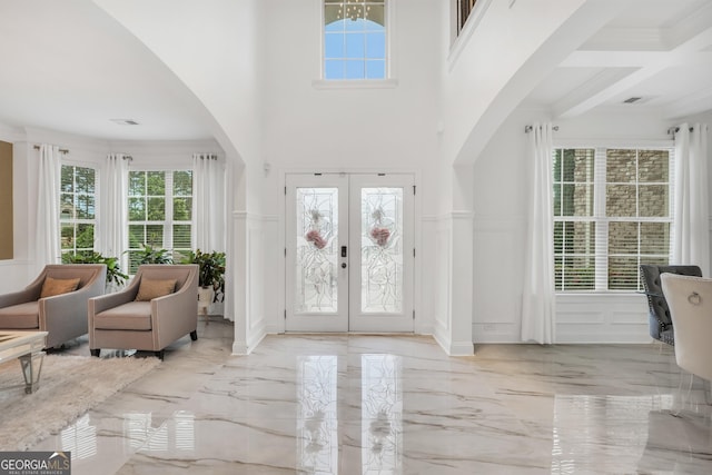 foyer entrance with marble finish floor, a decorative wall, a wainscoted wall, french doors, and arched walkways