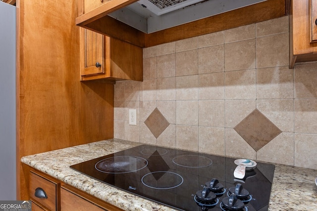 4577 San Saba Dr, Hahira, GA 31632 - kitchen with light stone counters, brown cabinetry, under cabinet range hood, and black electric stovetop