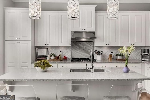3592 Parkhaven Pl, Brookhaven, GA 30319 - kitchen with decorative backsplash, a sink, a breakfast bar, under cabinet range hood, and white cabinetry