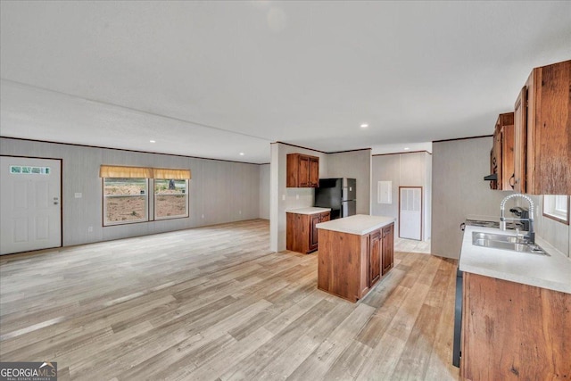 kitchen with a sink, brown cabinetry, light wood-style flooring, a center island, and freestanding refrigerator