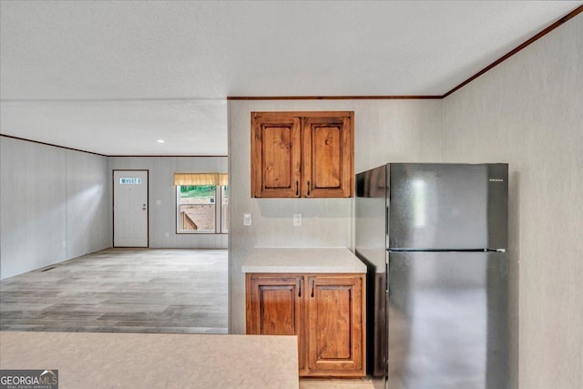 kitchen featuring freestanding refrigerator, brown cabinets, ornamental molding, and light countertops