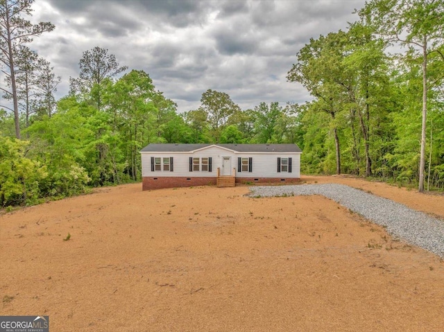 manufactured / mobile home with a view of trees, gravel driveway, and crawl space