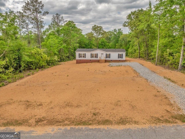 exterior space featuring gravel driveway, crawl space, and a wooded view