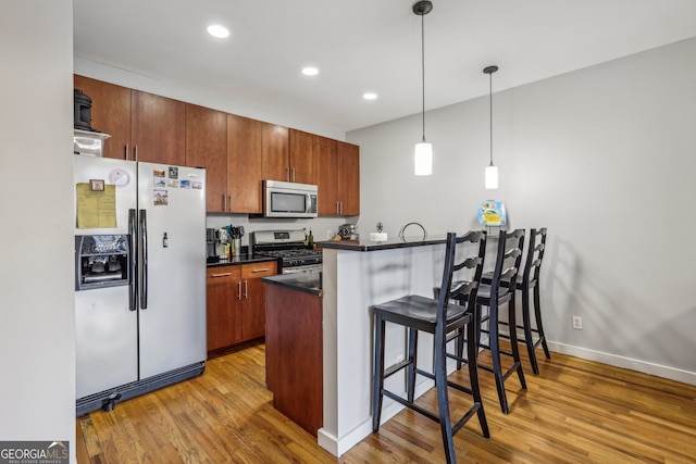 kitchen with stainless steel appliances, dark countertops, light wood-type flooring, and a kitchen bar