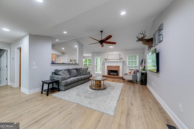 living area with light wood-style floors, baseboards, ceiling fan, and a fireplace with raised hearth