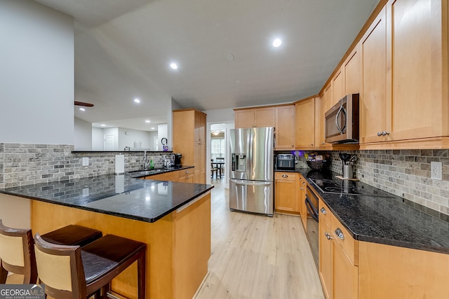 kitchen featuring light wood-style floors, decorative backsplash, black appliances, and a sink