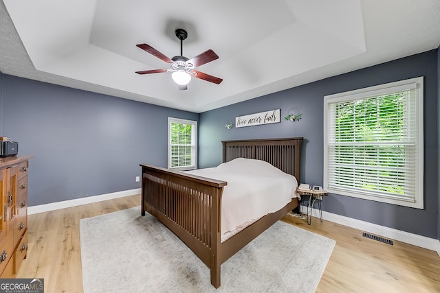 bedroom with visible vents, wood finished floors, baseboards, a raised ceiling, and a ceiling fan