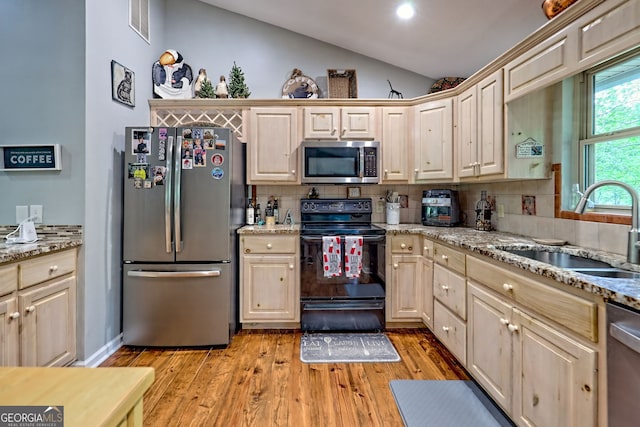 kitchen featuring decorative backsplash, light wood-style floors, a sink, vaulted ceiling, and stainless steel appliances