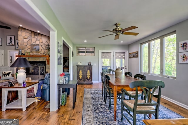 dining area with a stone fireplace, a ceiling fan, wood finished floors, and a healthy amount of sunlight