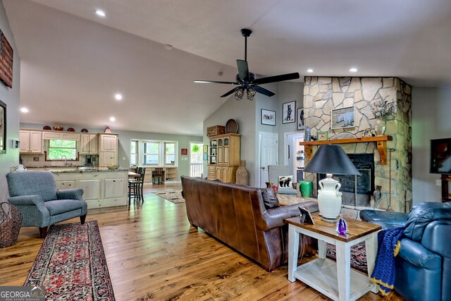 living area featuring lofted ceiling, a fireplace, recessed lighting, a ceiling fan, and light wood finished floors