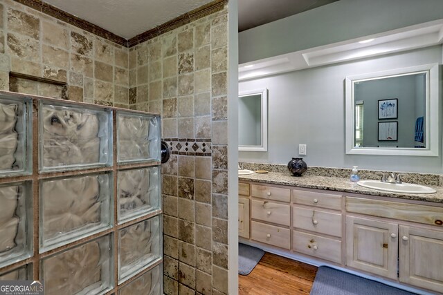 full bath featuring a walk in shower, double vanity, a sink, and wood finished floors