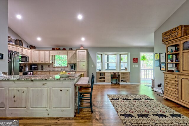 kitchen with a peninsula, light stone countertops, appliances with stainless steel finishes, and wood finished floors