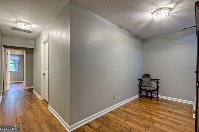 hallway with visible vents, a textured ceiling, baseboards, and dark wood-style floors