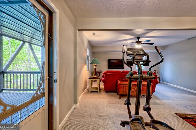 exercise area with baseboards, a textured ceiling, ceiling fan, and light carpet