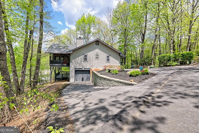 view of property exterior with a garage, a chimney, and driveway