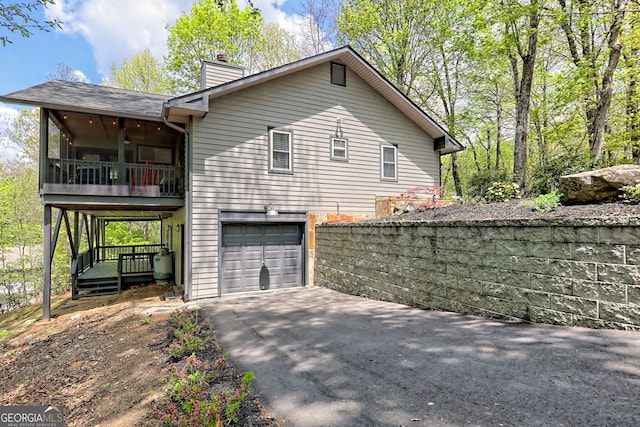 view of side of property featuring a sunroom, a chimney, an attached garage, and aphalt driveway