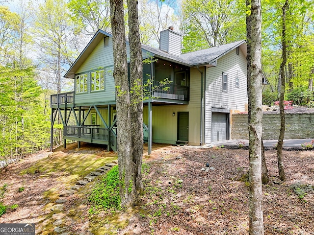 back of house featuring a shingled roof, an attached garage, a sunroom, a deck, and a chimney
