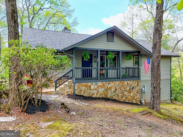 view of front of home with covered porch, a chimney, and roof with shingles