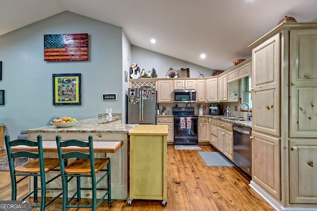 kitchen featuring lofted ceiling, light wood-style floors, a kitchen bar, a sink, and stainless steel appliances