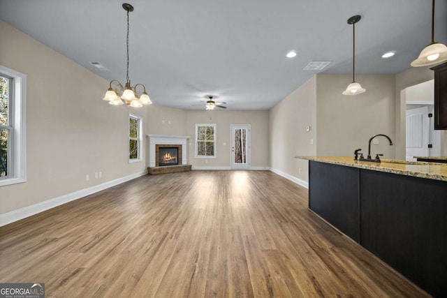 unfurnished living room featuring wood finished floors, a sink, baseboards, ceiling fan with notable chandelier, and a glass covered fireplace
