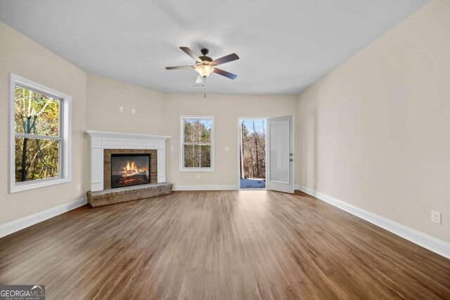 unfurnished living room with baseboards, a ceiling fan, wood finished floors, and a brick fireplace