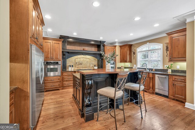 kitchen featuring light wood-style floors, ornamental molding, brown cabinets, and stainless steel appliances
