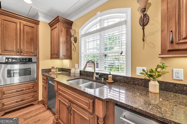 kitchen with dark stone counters, brown cabinets, a sink, light wood finished floors, and appliances with stainless steel finishes