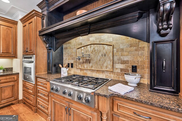 kitchen featuring brown cabinets, stainless steel appliances, decorative backsplash, and dark stone counters