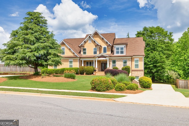 craftsman house with concrete driveway, brick siding, fence, and a front lawn