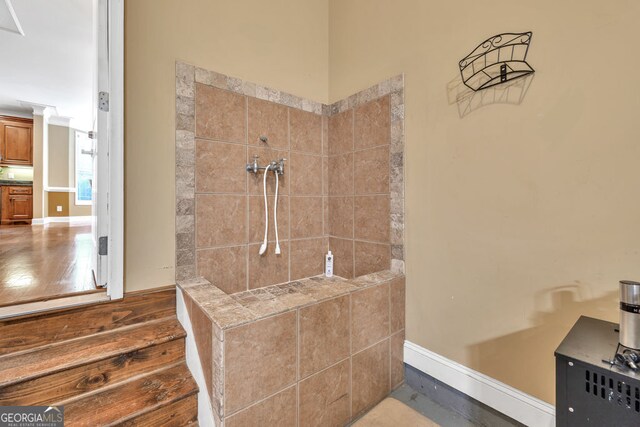 bathroom with baseboards, tiled shower, and wood finished floors