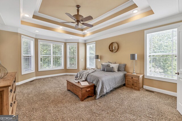 bedroom with light colored carpet, ornamental molding, a tray ceiling, and multiple windows