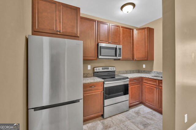 kitchen with stainless steel appliances, light stone counters, and brown cabinetry