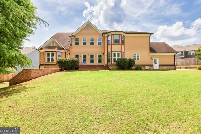 rear view of property featuring fence and a lawn