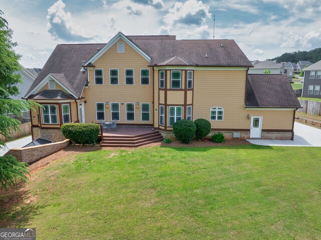 rear view of house with a shingled roof, a wooden deck, a yard, and fence