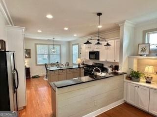 kitchen featuring black microwave, crown molding, wood finished floors, freestanding refrigerator, and a peninsula