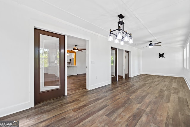 unfurnished living room with plenty of natural light, ceiling fan with notable chandelier, and dark wood-type flooring