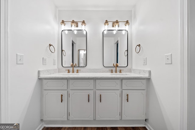 bathroom featuring baseboards, a sink, wood finished floors, and double vanity