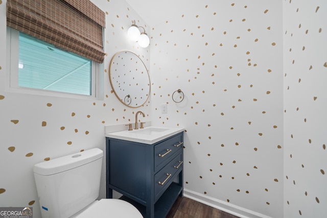 bathroom with vanity, wood finished floors, toilet, baseboards, and wallpapered walls
