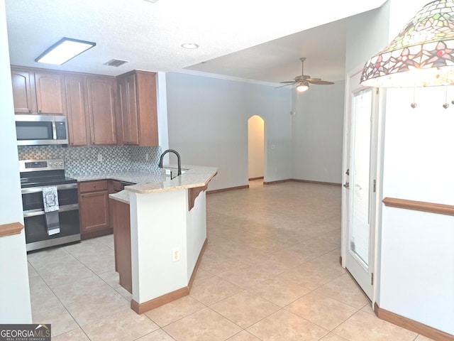 kitchen featuring arched walkways, stainless steel appliances, a ceiling fan, a peninsula, and tasteful backsplash